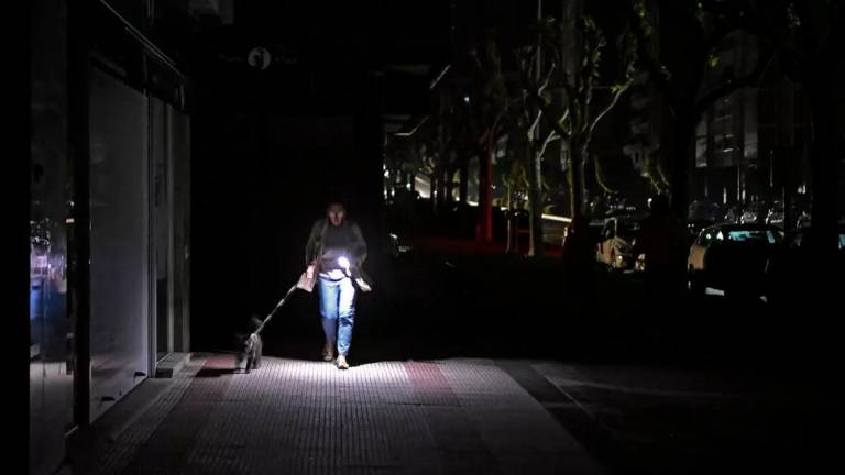 A woman uses her phone’s flashlight while she walks her dog in the dark during the massive power cut in Spain. © Miguel Riopa, AFP