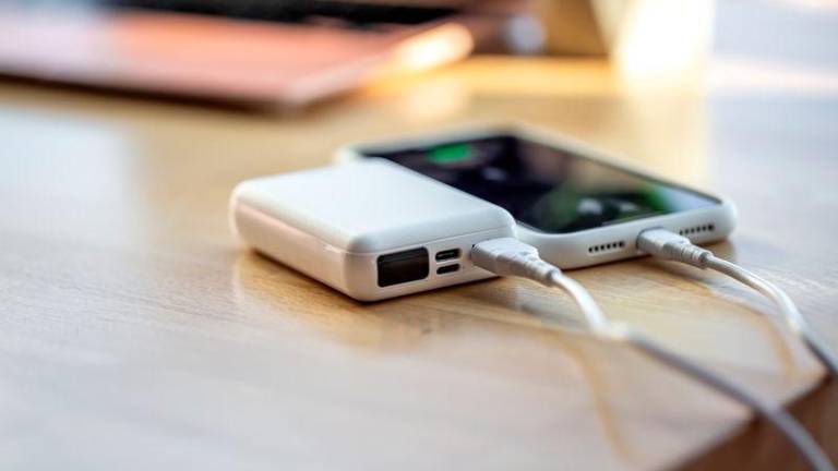 The smartphone is charged from a small white power bank via a cord.