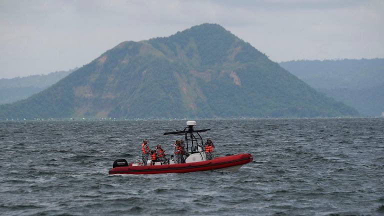 Philippine coast guard personnel aboard an inflatable boat speeds past one of Taal craters on their way to the site where the bodies of cockfighters were allegedly dumped in Taal Lake off Laurel town, Batangas province South of Manila on July 10, 2025. Search teams began scouring a lake south of the Philippine capital Manila for dozens of cockfighters allegedly murdered by rogue police. - Ted ALJIBE / AFP