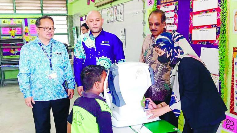 Ahmad Maswan (centre) watching a pupil undergoing eye screening.