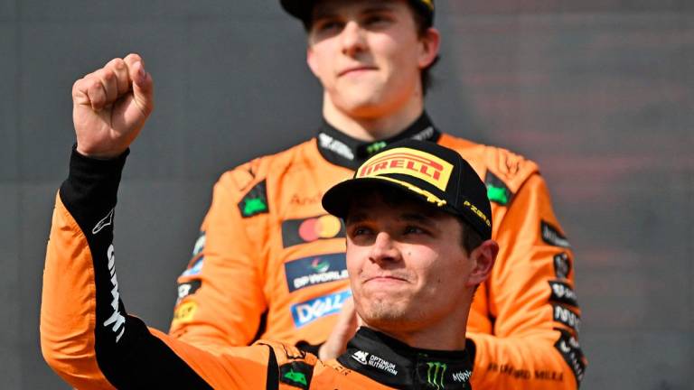 McLaren’s British driver Lando Norris celebrates on the podium after winning the Formula One Hungarian Grand Prix at the Hungaroring circuit in Mogyorod near Budapest, Hungary, on August 3, 2025; behind him in background can be seen second placed McLaren’s Australian driver Oscar Piastri. - Attila KISBENEDEK / AFP