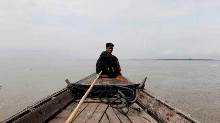 A man sits in a boat on the waters of the Brahmaputra river near the international border between India and Bangladesh in Dhubri district, in the northeastern state of Assam, India - REUTERSpix