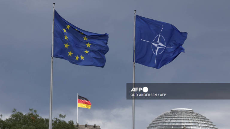 The EU, German and NATO flag fly backdropped by the Reichstag building that houses the Bundestag (lower house of Parliament) ahead a ceremony to mark Germany's 70 years in NATO in Berlin, on July 9, 2025. - AFP