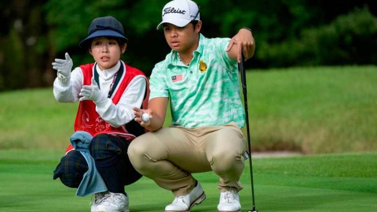 Malaysia’s Rizq Adam Rohizam reads a putt with the help of his caddie