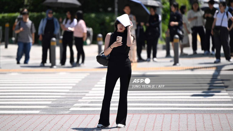 A woman uses a piece of paper to shade herself from the sun as she waits to cross a road in Seoul on July 10, 2025, as a heat wave warning has been issued by the South Korean government. - AFP