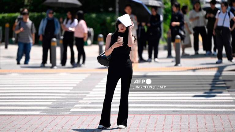 A woman uses a piece of paper to shade herself from the sun as she waits to cross a road in Seoul on July 10, 2025. - Jung Yeon-je / AFP