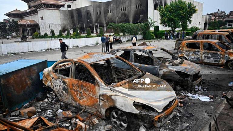 A man walks past the remains of charred vehicles at the parking lot of the torched Parliament building in Kathmandu on September 14, 2025. Nepal’s new leader Sushila Karki vowed on September 14, to follow protesters’ demands to “end corruption” as she began work as interim prime minister, after “Gen Z” youth demonstrations ousted her predecessor. (Photo by Pedro PARDO / AFP)