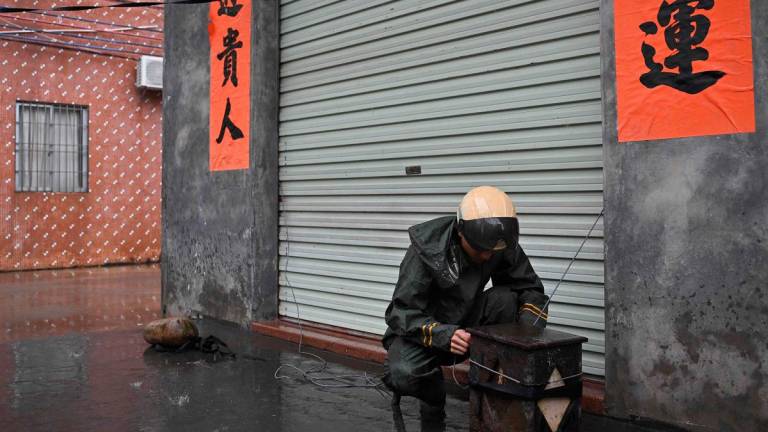 A man ties down the shutters of his premises onto a weight during the passing of Super Typhoon Ragasa in Yangjiang, southern China’s Guangdong province on September 24, 2025. - ADEK BERRY / AFP