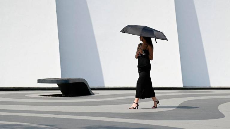 A woman holding an umbrella to shelter from the sun walks along a street in Beijing on June 23, 2025 - WANG Zhao / AFP