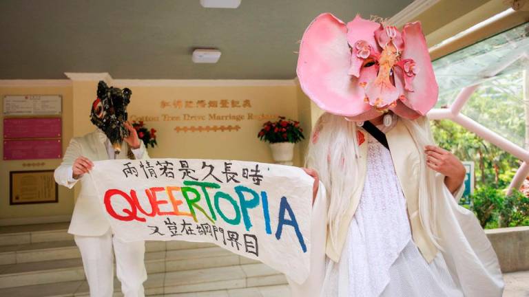 This photo taken on July 28, 2025 shows non-binary performance artist Holok Chen (R) and a model who requested anonymity holding a banner that reads “If the love is meant to endure, why should it be confined to portals and digital boundaries” as they promote LGBTQ equality outside the Cotton Tree Drive Marriage Registry in Hong Kong. Hong Kong’s LGBTQ community has reluctantly rallied behind a government plan that could expand rights for same-sex couples, with “desperate” activists ditching their idealism in hopes of a rare legislative win. - May JAMES / AFP