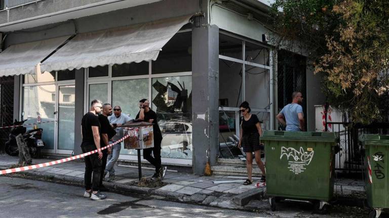 People stand next to a damaged shop following a strong blast in Thessaloniki on July 26, 2025. A strong blast early on July 26, 2025 damaged an apartment building in a suburb of Greece's second city Thessaloniki, wounding two passersby and shattering windows of nearby buildings. - AFPPIX