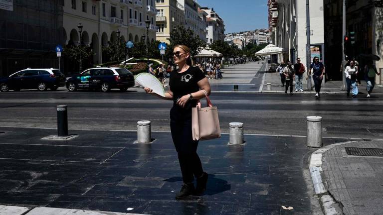 A woman cools down with a hand fan in the centre of Thessaloniki on July 20, 2025. (Photo by Sakis Mitrolidis / AFP)