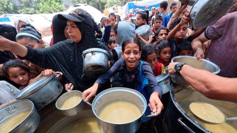 Palestinian children line up to receive a hot meal at a food distribution point in Nuseirat on June 30, 2025. (Photo by Eyad BABA / AFP)