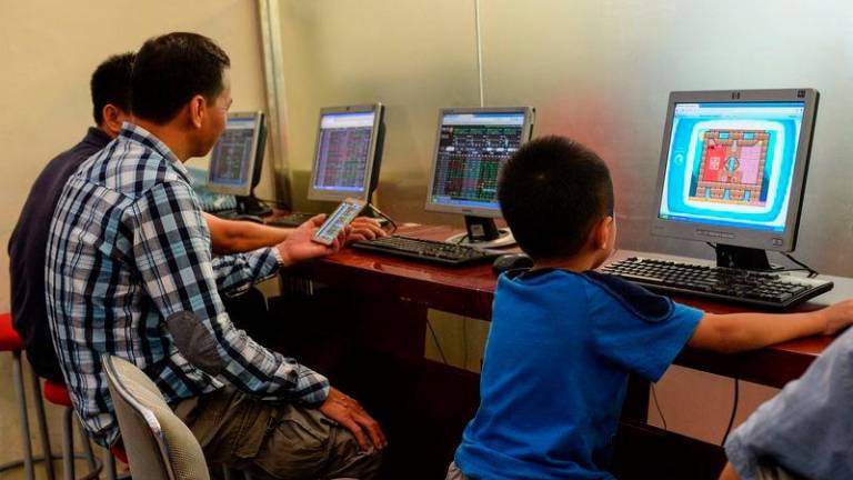 A child plays a game on a computer as investors look at share prices at a securities firm in Hanoi - AFPpix