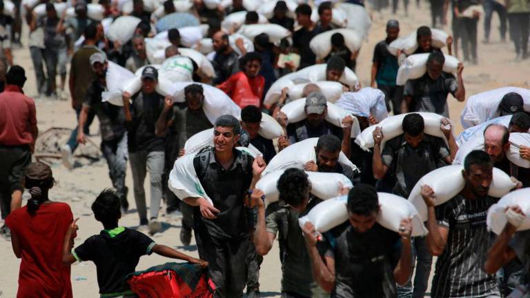 Palestinian walk carrying sacks of flour near Jabalia, in the northern Gaza Strip, on July 27, 2025, after planes dropped aid into Gaza. (Photo by BASHAR TALEB / AFP)