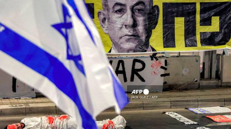 A demonstrator lies on the ground while depicting an Israeli hostage during an anti-government protest organised by the families of the Israeli hostages taken captive in the Gaza Strip since the October 2023 calling for action to secure their release and a ceasefire in the war against Hamas outside the Defence Ministry headquarters in Tel Aviv on August 23, 2025. - AFP