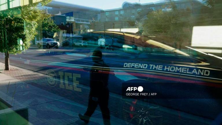 An ICE promotional car sits in a lobby as a man is reflected in a window as he walks to attend an ICE recruitment job fair at the Utah Valley Convention Center in Provo, Utah on September 15, 2025. - AFP