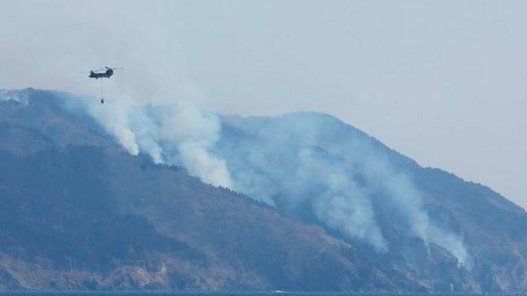 A helicopter is pictured as smoke rises due to a wildfire on a mountainside near the city of Ofunato, Iwate Prefecture - AFPpix