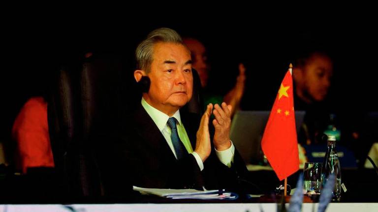 China's Foreign Minister Wang Yi (C) reacts as unseen South African President Cyril Ramaphosa delivers the keynote address at the welcome ceremony during the G20 Foreign Minister Meeting at the Nasrec Expo Centre in Johannesburg on February 20, 2025. - AFPPIX