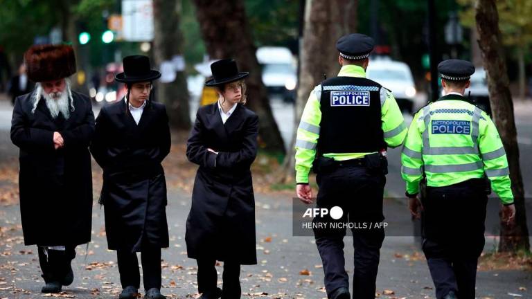 Members of the local Jewish community look on as police officers patrol the streets in Stanford Hill, north London on October 2, 2025. - AFP