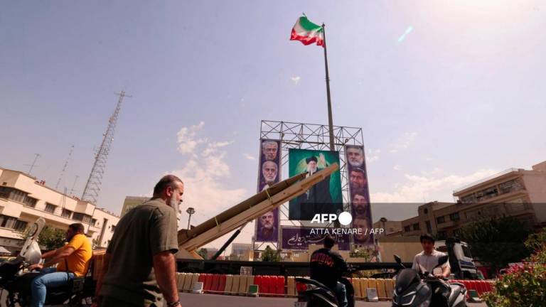 Iranians ride their motorcycles past a deactivated Kheibar Shekan ballistic missile in front of a picture of Iran's Supreme Leader Ayatollah Ali Khamenei in Tehran's Bahrestan Square on September 27, 2025, as part of an exhibit to mark the Sacred Defense Week commemorating the 1980-88 Iran-Iraq war. - AFPPIX
