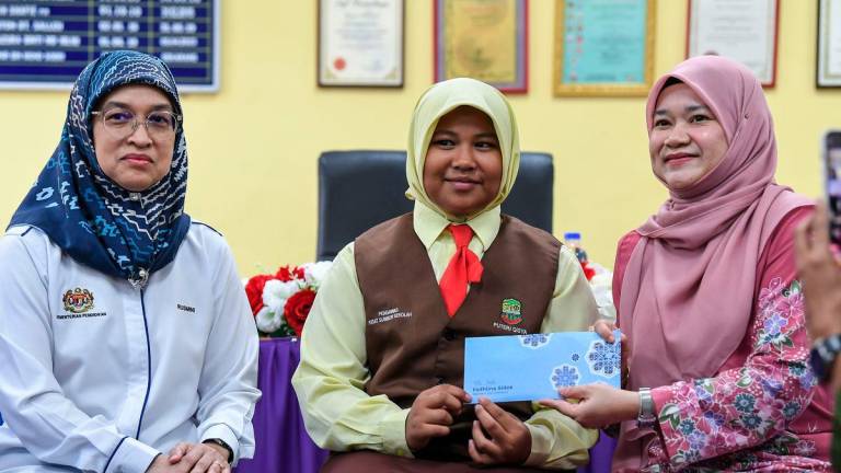 Education Minister Fadhlina Sidek presents a contribution to 12-year-old Putri Qisya Nur Izzat, who lost her entire family in last week’s Sungai Korok tragedy, during a visit to offer support - Photo by BERNAMA