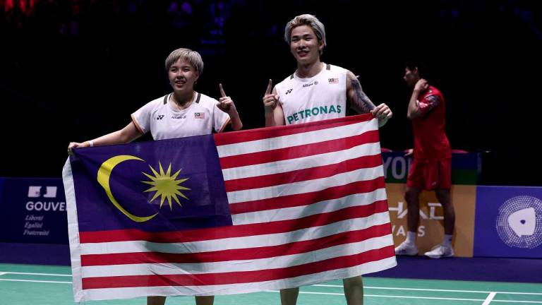 Chen Tang Jie and Toh Ee Wei (L) hold their national flag as they celebrate beating China’s Jiang Zhen Bang and Wei Ya Xin in the mixed doubles final match at the Badminton BWF World Championships at the Adidas Arena in Paris, on August 31, 2025. - Thibaud MORITZ / AFP