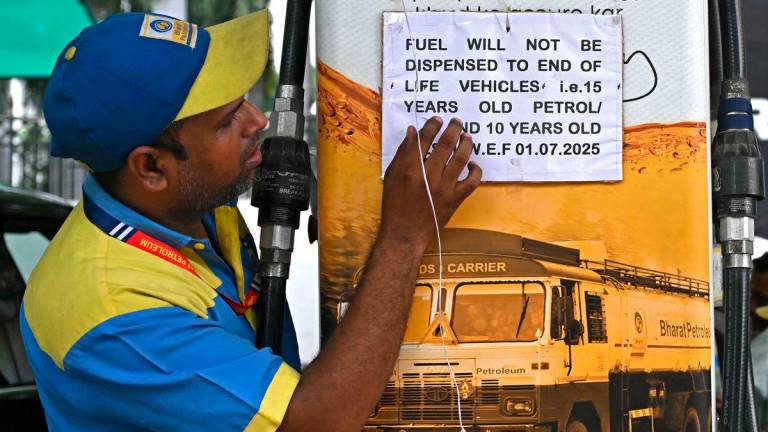 A fuel attendant displays a notice announcing the ban on refuelling petrol cars older than 15 years and diesel vehicles older than 10 years, displayed at a gas station in New Delhi on July 1, 2025. (Photo by Arun SANKAR / AFP)