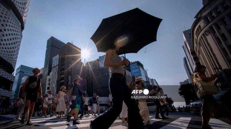 People cross a street on a hot day in Tokyo on August 4, 2025. - AFP
