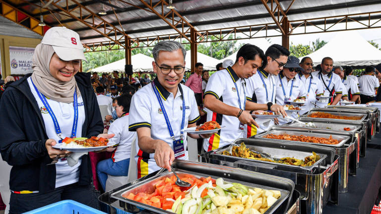 Menteri Komunikasi Datuk Fahmi Fadzil (dua, kiri) mengambil juadah yang dimasak secara gotong-royong oleh penduduk setempat pada Program Ukhwah Kepimpinan MADANI di Dataran Kampung Pachitan hari ini. - BERNAMA