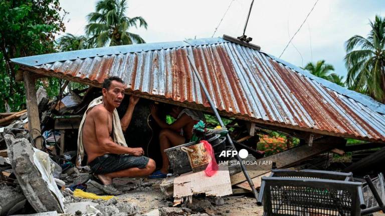 Men look for items in a collapsed house in Manay, in the province of Davao Oriental on October 11, 2025, after two powerful quakes struck off the southern Philippines on October 10, killing at least eight people and triggering tsunami warnings. - AFP