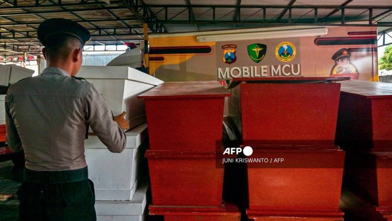A Police officer stacks coffins for victims of a building collapse at the Al Khoziny Islamic boarding school, at the Bhayangkara hospital in Surabaya, East Java province on October 4, 2025. - AFP