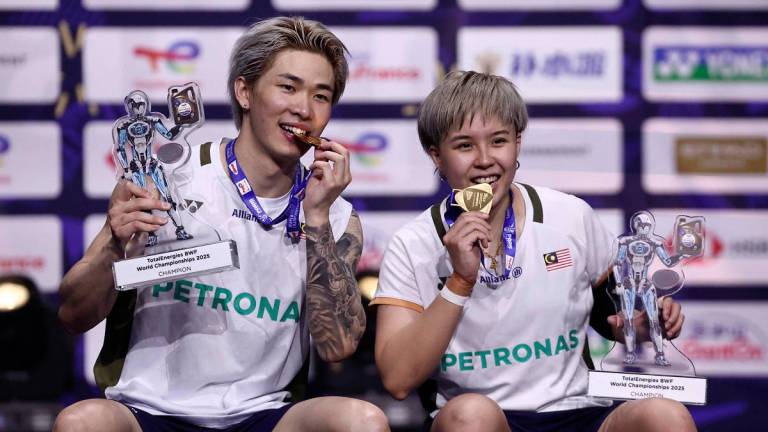 Malaysia’s Chen Tang Jie (L) and Toh Ee Wei hold their trophies as they bite their medals as they celebrate on the podium after beating China’s Jiang Zhen Bang and Wei Ya Xin in the mixed doubles final match at the Badminton BWF World Championships at the Adidas Arena in Paris, on August 31, 2025. - Thibaud MORITZ / AFP