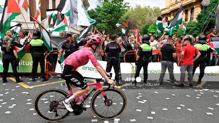 A cyclist competes as pro-Palestinian protesters holding Palestinian and Basque flags demonstrate during the eleventh stage of the Vuelta a Espana cycling tour, a 167 km race from Bilbao to Bilbao, on September 3, 2025. - AFP