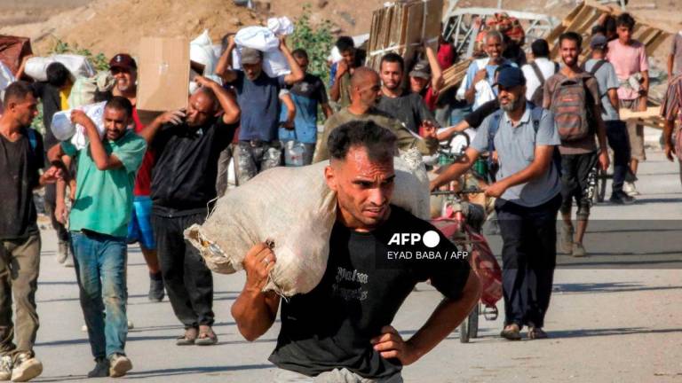 People walk with bags of humanitarian aid they received at a distribution centre run by the US and Israeli-backed Gaza Humanitarian Foundation (GHF), as they cross the so-called Netzarim corridor in the central Gaza Strip, on August 22, 2025. - AFP