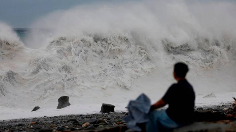 A woman sits by the shore while looking at waves breaking as Typhoon Koinu approaches, in Taitung, Taiwan October 4, 2023. - REUTERS/Carlos Garcia Rawlins