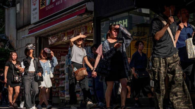 People shield their eyes from the sun as they walk through a street on a hot day in Tokyo on July 26, 2025. - AFPPIX
