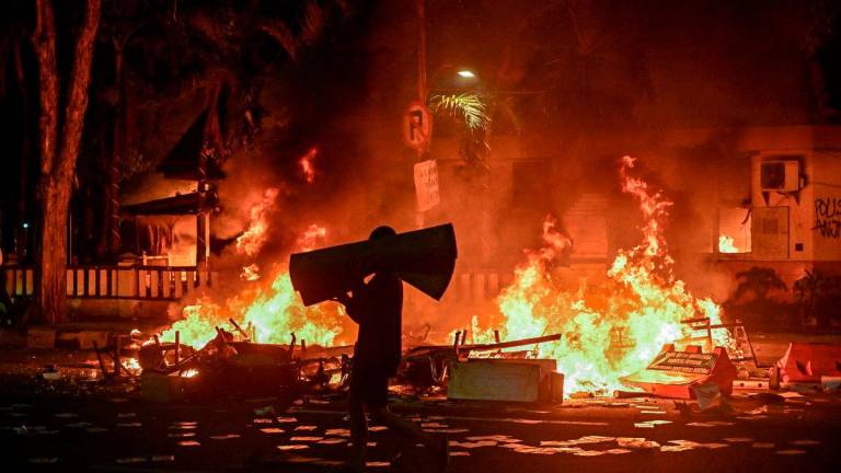 A protester carries looted goods on a street in front of a police headquarters that was set on fire and looted during demonstrations in Surabaya on August 31, 2025. Southeast Asia’s biggest economy has been rocked by protests in major cities, including the capital Jakarta, since April 29 after footage spread of a motorcycle taxi driver being run over by a police tactical vehicle during an earlier rally against low wages and financial perks for lawmakers. (Photo by Juni KRISWANTO / AFP)