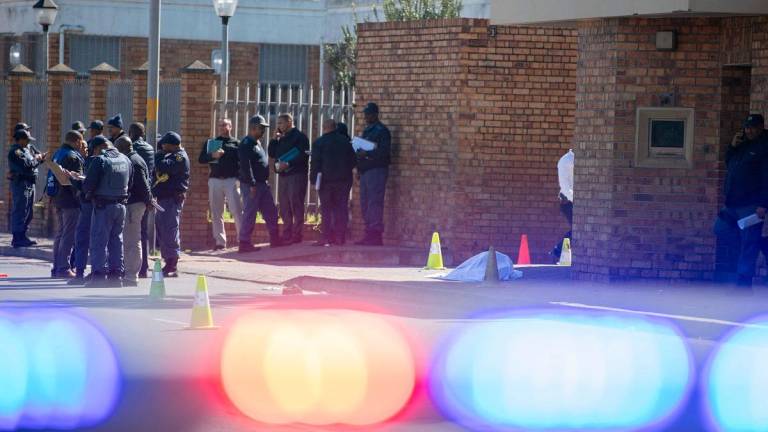 Members of the South African Police Services (SAPS) stand next to the body of a young man who had been shot shortly before outside the Mitchells Plain Magistrates Court near Cape Town on August 25, 2025. - RODGER BOSCH / AFP