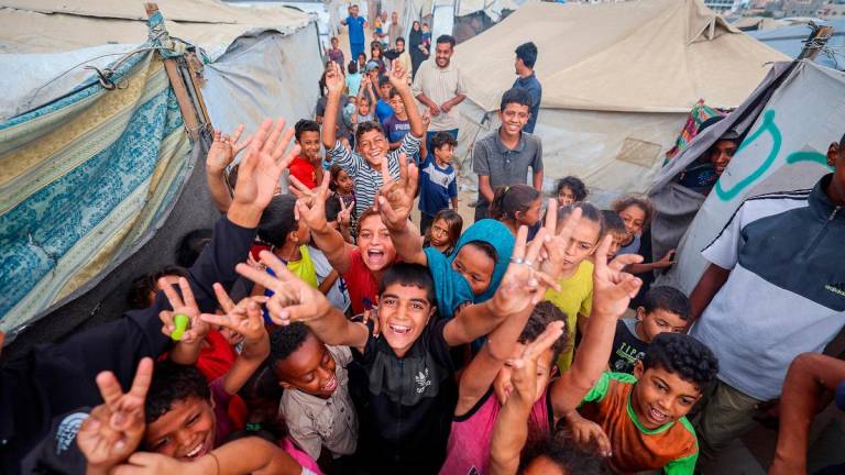 Palestinian children celebrate at a camp for displaced people in Nuseirat in the central Gaza Strip on October 9, 2025, following news of a new Gaza ceasefire deal. - Eyad BABA / AFP