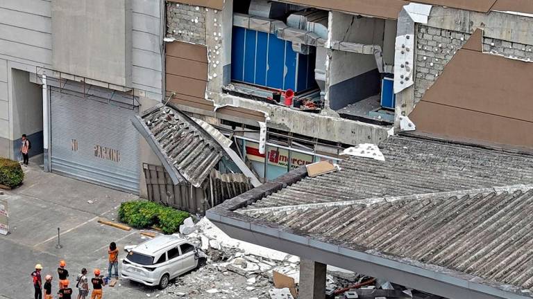 Authorities inspect a damaged wall and a car outside a mall in Butuan City, on the southern island of Mindanao on October 10, 2025, after a 7.4-magnitude earthquake struck off the southern Philippines. - Erwin MASCARINAS / AFP