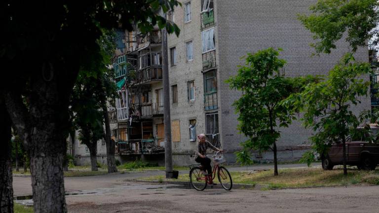 A woman rides a bicycle past a damaged residential building in the town of Lyman, near the frontline in the Donetsk region on June 24, 2025, amid the Russian invasion of Ukraine. (Photo by Tetiana DZHAFAROVA / AFP)