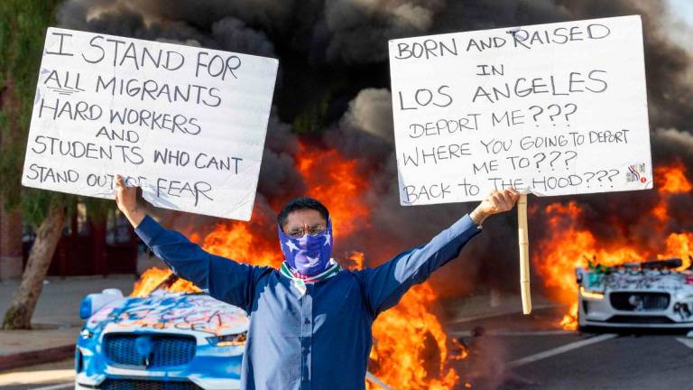 A man holds signs as a Waymo vehicles burn, as protesters clash with law enforcement in the streets surrounding the federal building during a protest following federal immigration operations in Los Angeles, California, on June 8, 2025.