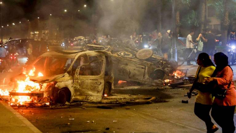 Women walk past police vehicles set on fire during a youth-led demonstration demanding reforms in the healthcare and education sectors in Sale on October 1, 2025. (Photo by Abdel Majid BZIOUAT / AFP)