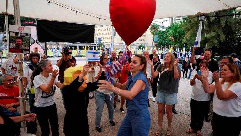 A person wearing a mask depicting U.S. President Donald Trump holds an Israeli flag and a heart-shaped ballon, as people celebrate after Trump announced that Israel and Hamas agreed on the first phase of a Gaza ceasefire, at the “Hostages square”, in Tel Aviv, Israel, October 9, 2025. REUTERS/Ronen Zvulun