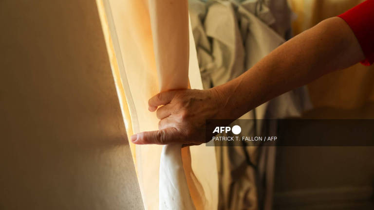 An undocumented immigrant from Honduras holds the curtain on her window after receiving a bag of groceries from the CLEAN Carwash Worker Center, which helps immigrants afraid to leave their homes due to fears of federal immigration raids and deportation, in Los Angeles, in Los Angeles, California on July 25, 2025. - AFP