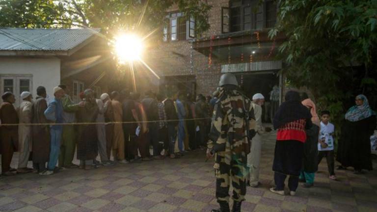 An Indian security personnel stands guard as voters queue up to cast their ballots at a polling station during the first phase of assembly elections in Pulwama, south of Srinagar on September 18, 2024. - AFPPIX