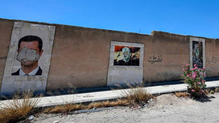 Defaced portraits of Syria’s ousted president Bashar al-Assad (L) and his late father Hafez al-Assad (C) hang on a wall in the capital Damascus on June 2, 2025. (Photo by LOUAI BESHARA / AFP)