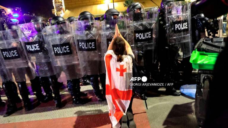 A protester wrapped in a Georgian flag gestures in front of riot police during an opposition rally on the day of local elections in central Tbilisi on October 4, 2025. - AFP