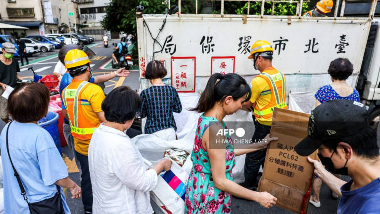This photo taken on June 19, 2025 shows residents folding cardboard boxes for recycling next to a collection truck in Taipei. Taiwanese residents holding plastic bags of rubbish stand on a footpath as a yellow garbage truck playing classical music over a loudspeaker pulls up. For decades, the tinkling of Beethoven's Fur Elise or Tekla Badarzewska-Baranowska's Maiden's Prayer has alerted Taiwanese households to take out their garbage. -AFP